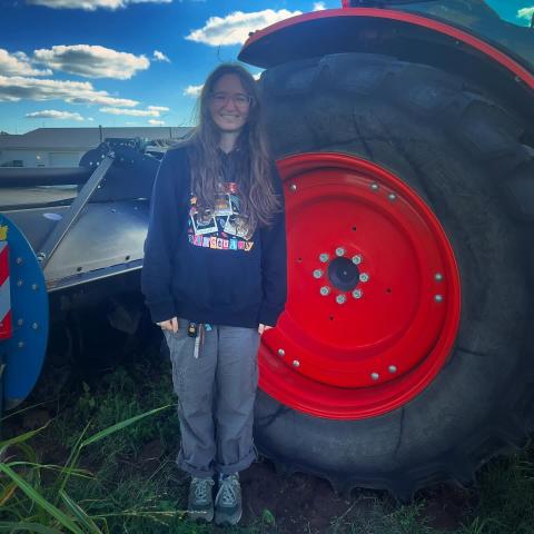 An apprentice stands with the biggest tractor on the farm